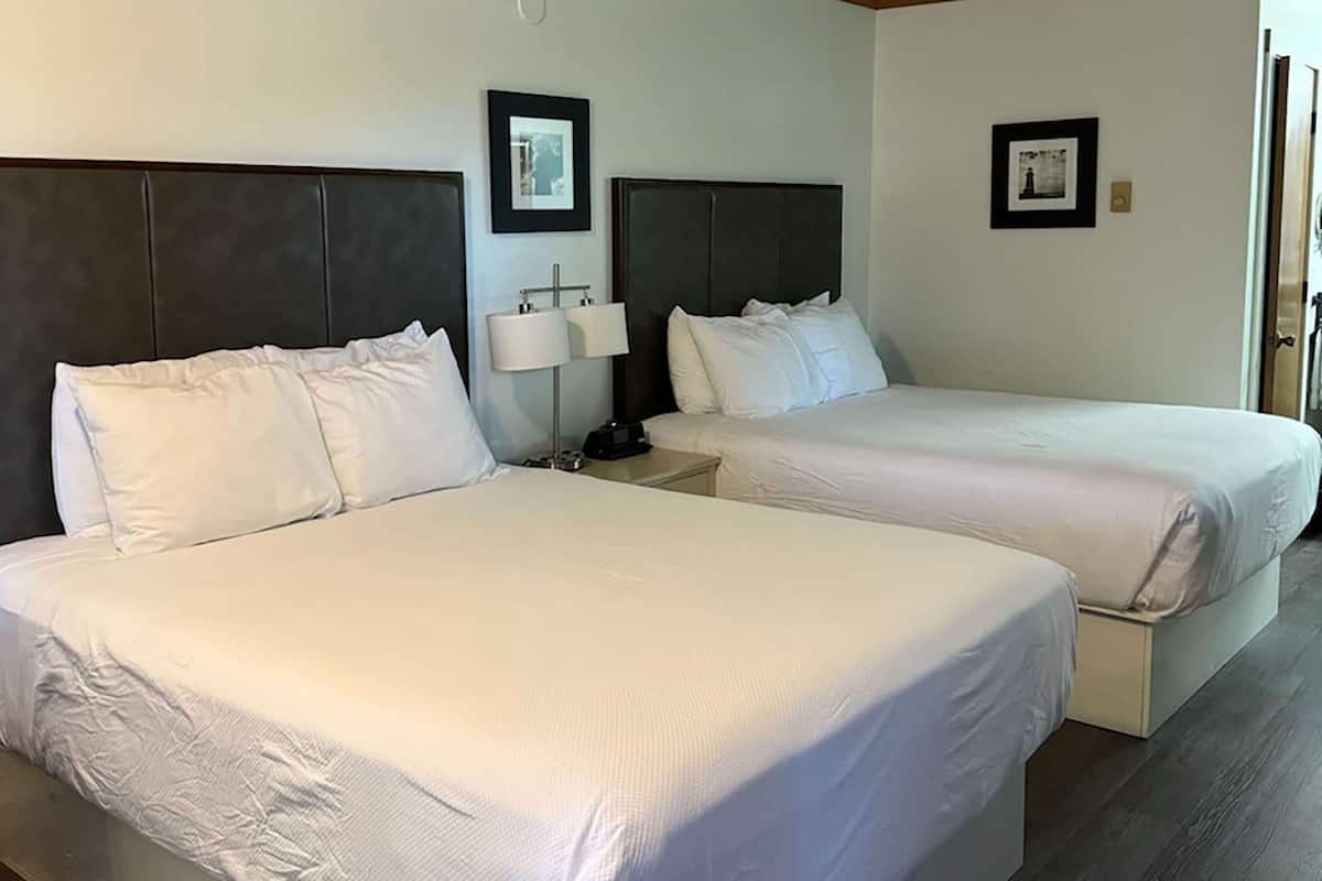 Ein Hotelzimmer mit zwei Betten, einem Nachttisch mit Lampe und gerahmten Bildern an der Wand.