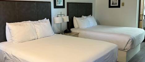 A hotel room with two beds, a bedside table with a lamp, and framed pictures on the wall.