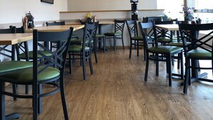 A restaurant interior with wooden ceiling, green cushioned chairs, wooden tables, framed artwork on the wall, and an exit sign.