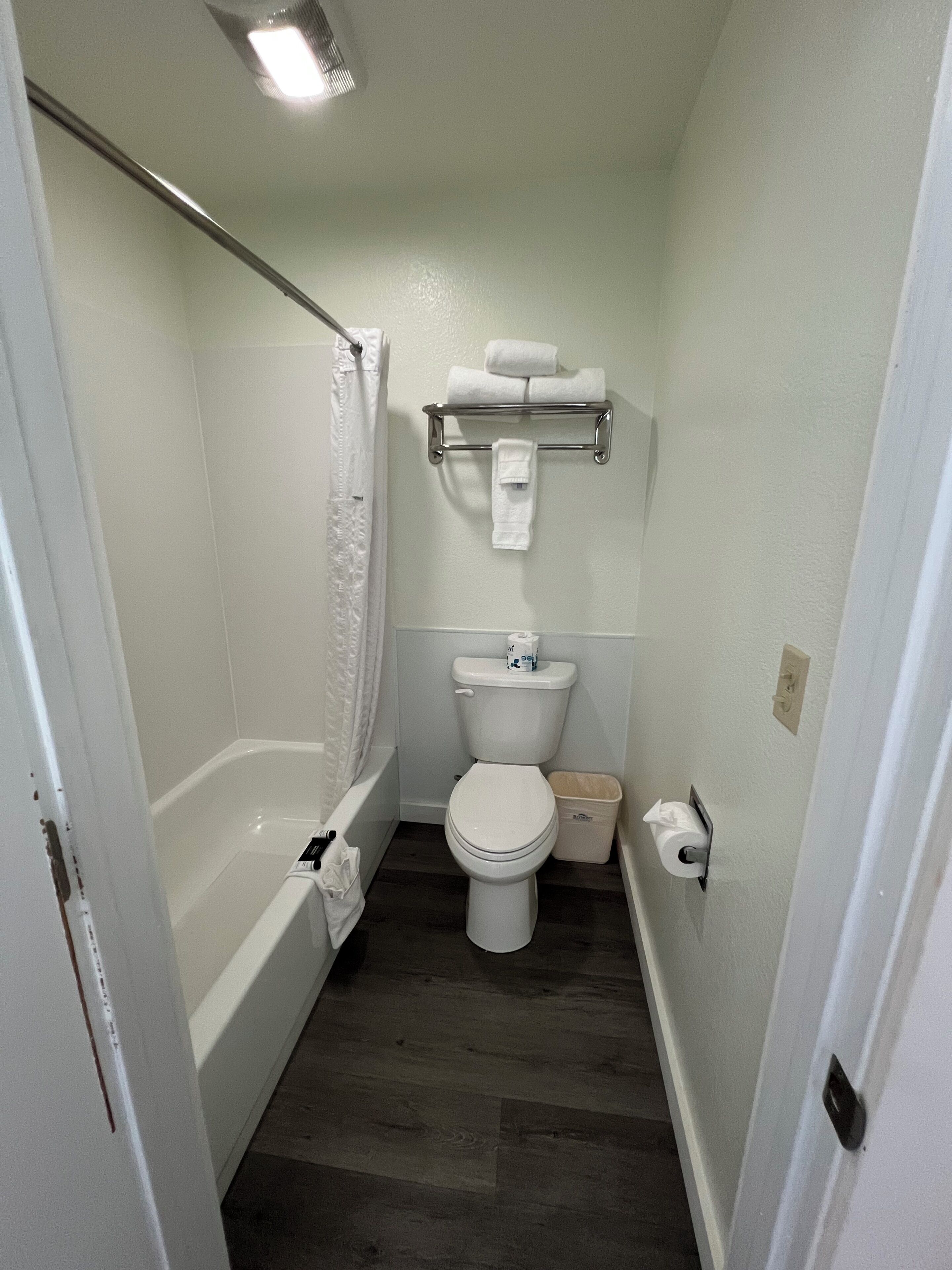 Une petite salle de bain étroite, équipée de toilettes, d’une douche et d’un porte-serviettes.