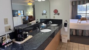 A hotel bathroom with a double sink, a large mirror, a coffee maker, and a towel rack.