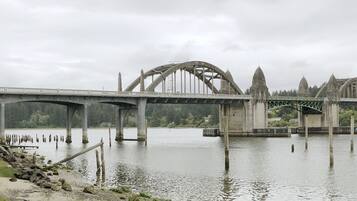 A large stone bridge with multiple arches over a calm river, surrounded by greenery and a small building with a balcony.