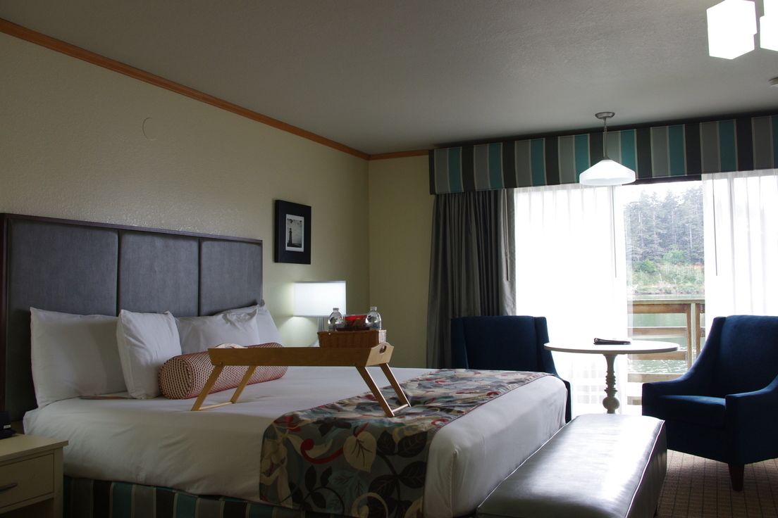 A hotel room with a bed, a bedside table, a chair, a small round table, and a window with curtains.