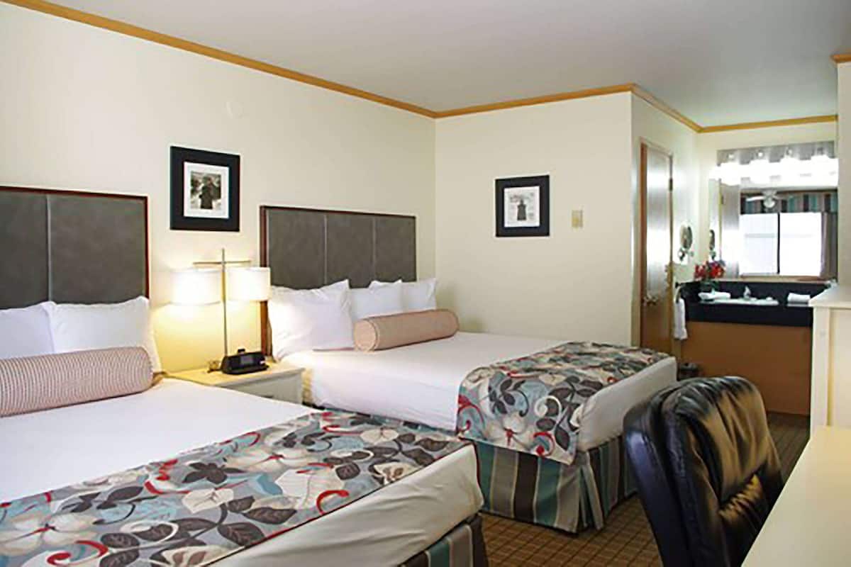 Ein Hotelzimmer mit zwei Betten, einem Schreibtisch, einem Stuhl und einem durch eine offene Tür einsehbaren Badezimmer.