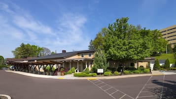 A hotel with a covered outdoor area, a parking lot, and a building with a green lawn.