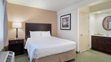 A hotel room with a bed, a nightstand with a lamp, a dresser, and a bathroom with a mirror.