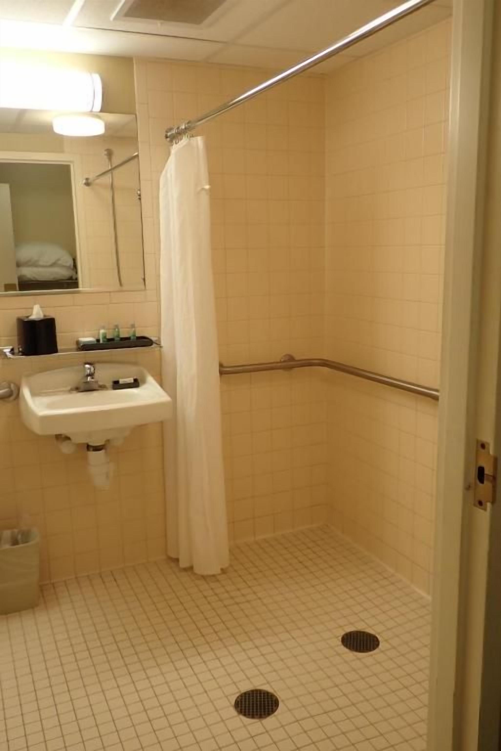 A small, tiled bathroom with a shower, a sink, and a mirror.