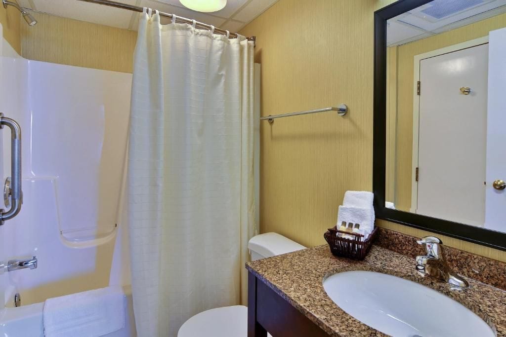 A bathroom with a shower, toilet, sink, and a mirror.