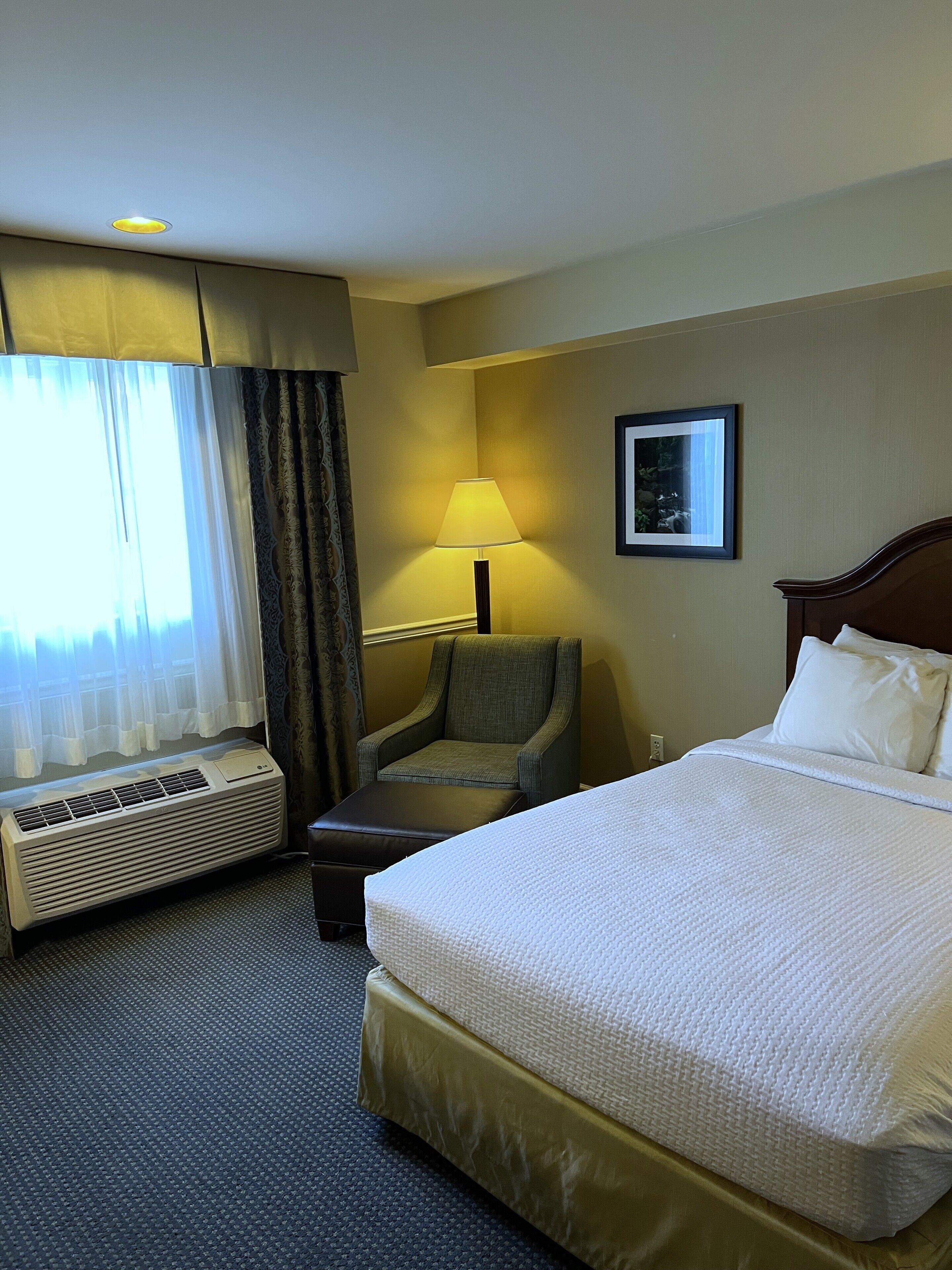 Une chambre d’hôtel avec un lit, une chaise, un bureau et une fenêtre avec des rideaux.