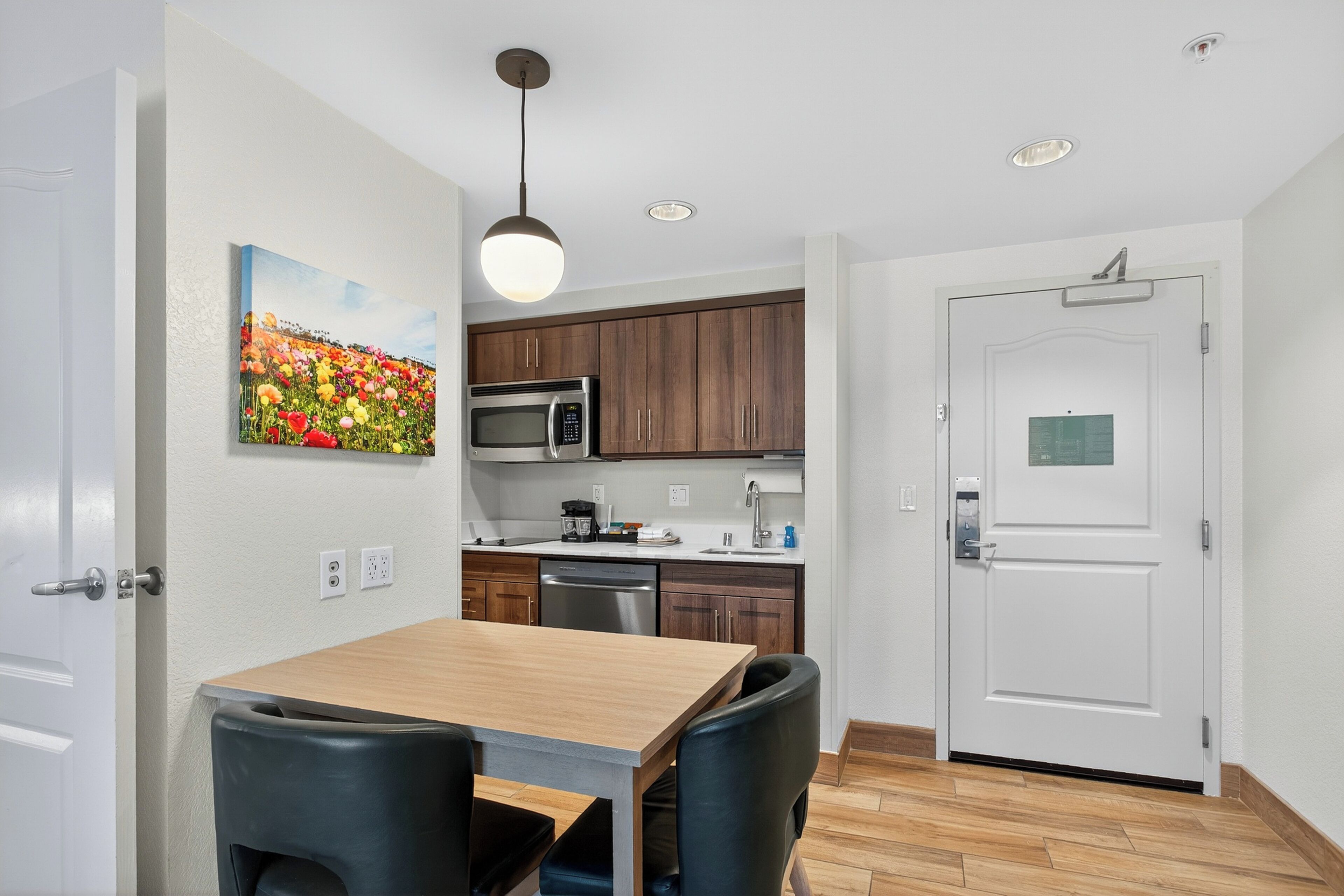A modern kitchen with wooden cabinets, a stainless steel microwave, and a wooden dining table with black chairs.
