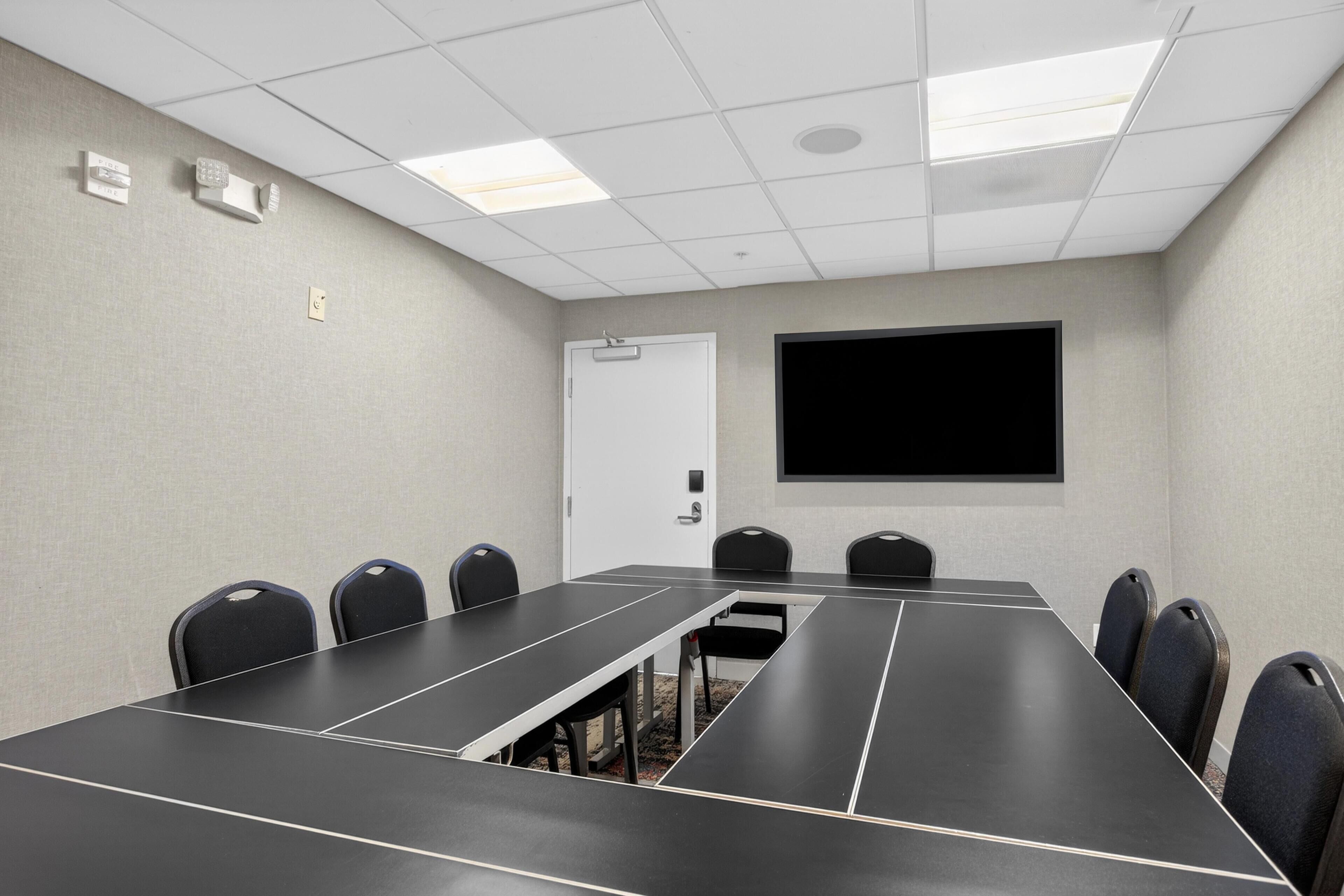 A conference room with a long table, chairs, a projector screen, and a door.