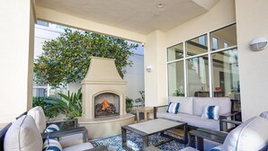 An outdoor patio with a fireplace, seating area, and large windows.