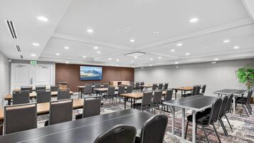 A conference room with multiple tables and chairs, a large painting on the wall, and an exit door.