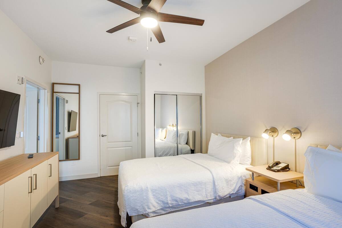 A hotel room with two beds, a ceiling fan, bedside lamps, a telephone, and a mirror.