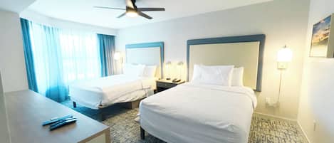 A hotel room with two beds, a desk, a ceiling fan, and a patterned carpet.