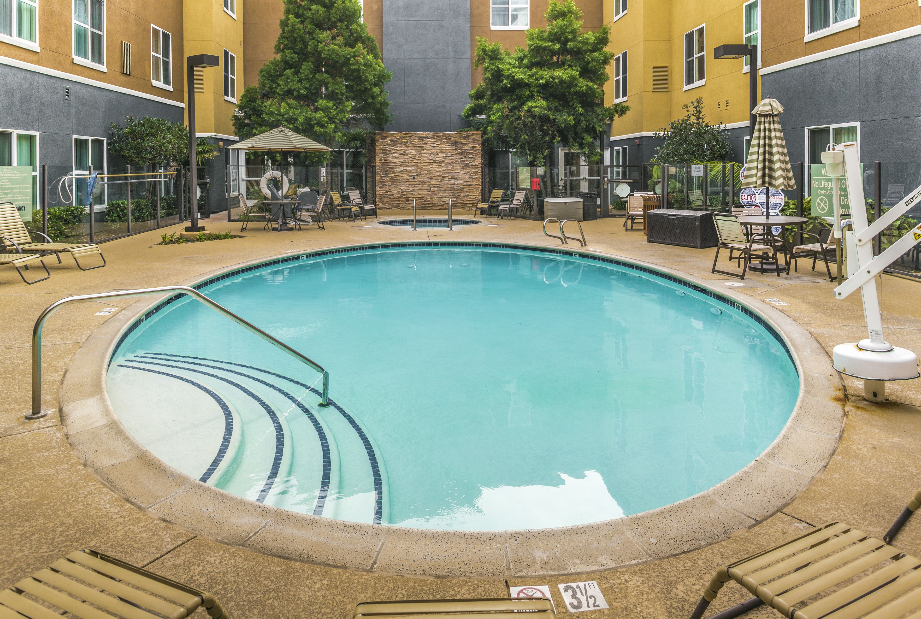 A swimming pool with a stone border, surrounded by lounge chairs and a covered seating area.