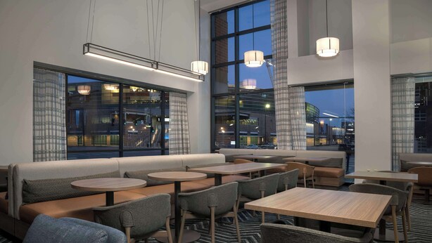 Un espace de détente intérieur moderne, doté de tables et de chaises, de grandes fenêtres et offrant une vue sur le paysage urbain.