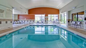 Une grande piscine intérieure à l’eau claire, entourée de fauteuils et de chaises longues.