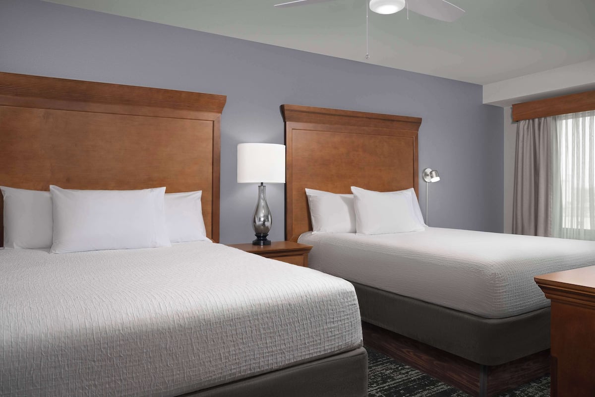 A hotel room with two beds, a ceiling fan, a bedside lamp, and a window with curtains.