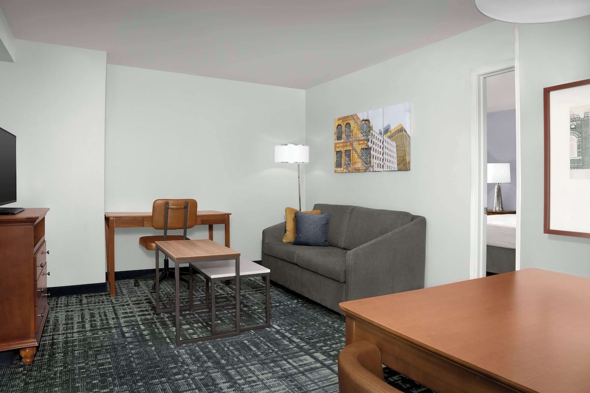 A hotel room with a desk, chair, sofa, and a television.