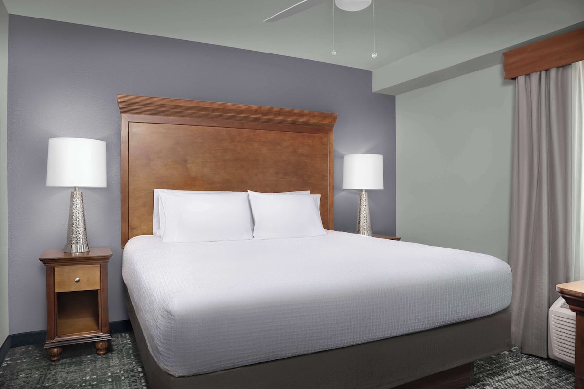 A hotel room with a large bed, two bedside tables with lamps, a wooden headboard, and a window with curtains.