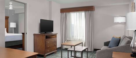 A hotel room with a bed, a TV, a desk, a sofa, and a window with curtains.