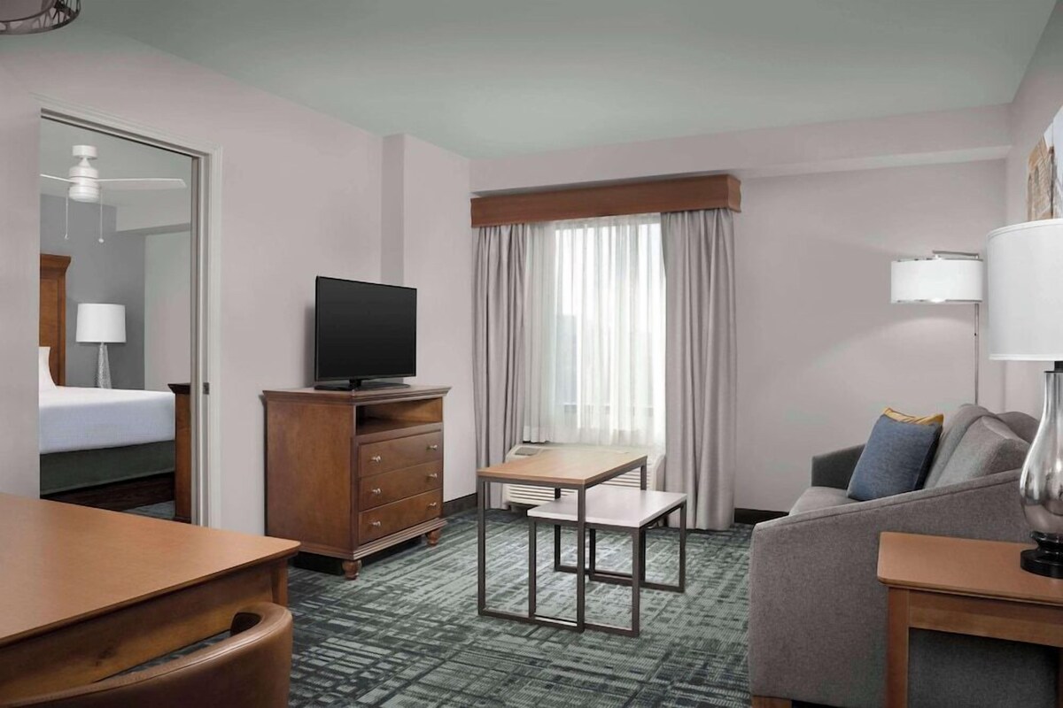 Une chambre d’hôtel avec un lit, une télévision, un bureau, un canapé et une fenêtre avec des rideaux.