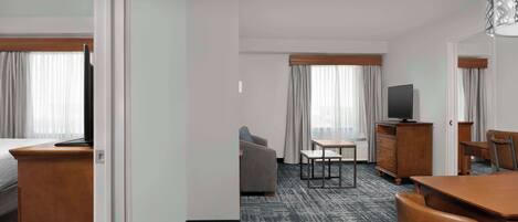A hotel room with a bed, a desk, a chair, a sofa, a TV, and a dresser.