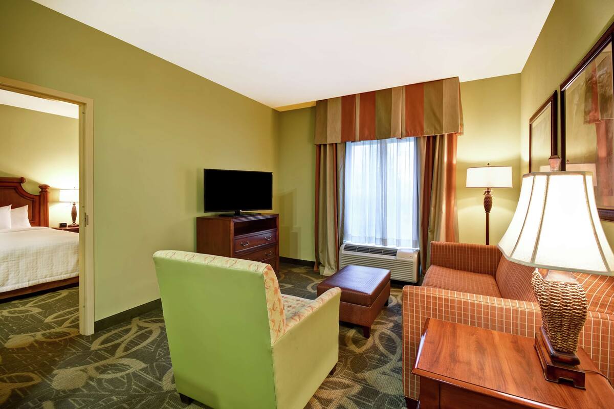 Habitación de hotel con cama, televisión, sofá, sillón, mesa y aire acondicionado.
