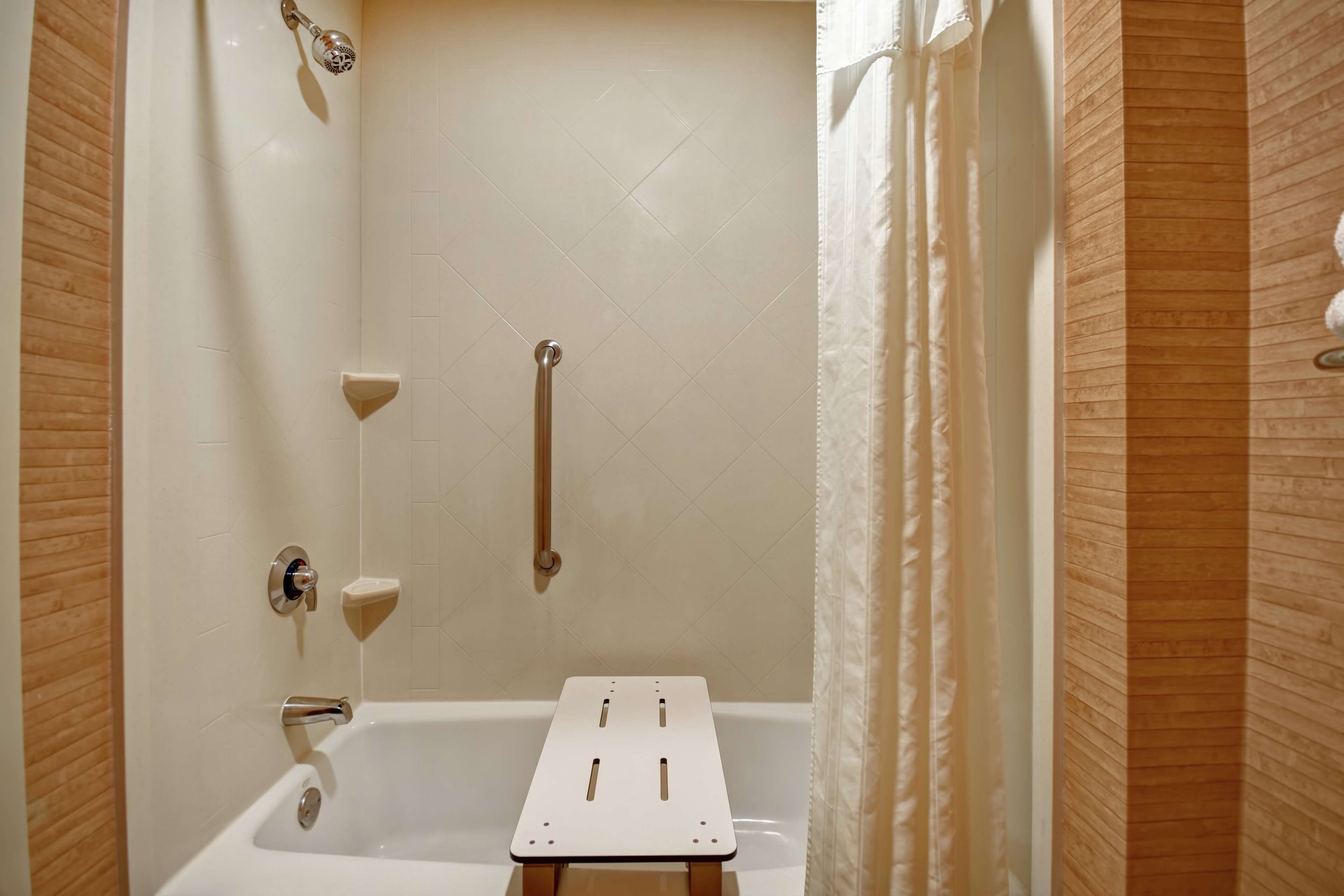 A bathroom with a white bathtub, a shower with a handheld showerhead, and a grab bar.