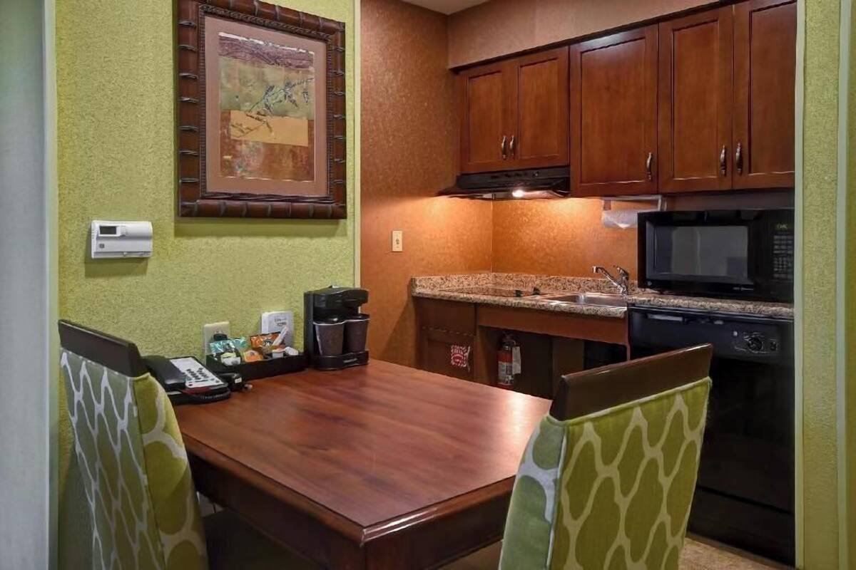 Cocina compacta con armarios de madera, microondas, estufa y cafetera sobre la encimera.