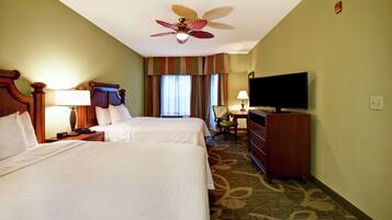A hotel room with two beds, a ceiling fan, a television, a desk with a chair, and a dresser.