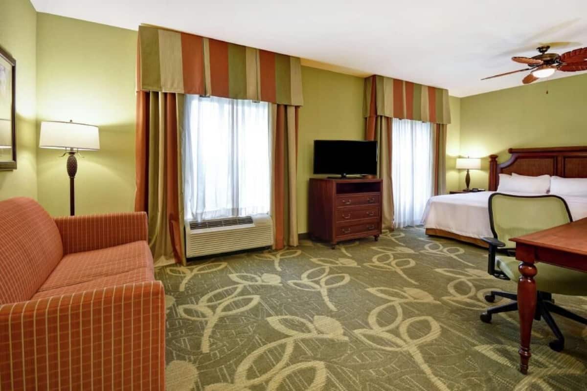 Una habitación de hotel con cama, escritorio, televisor, sofá y ventilador de techo.