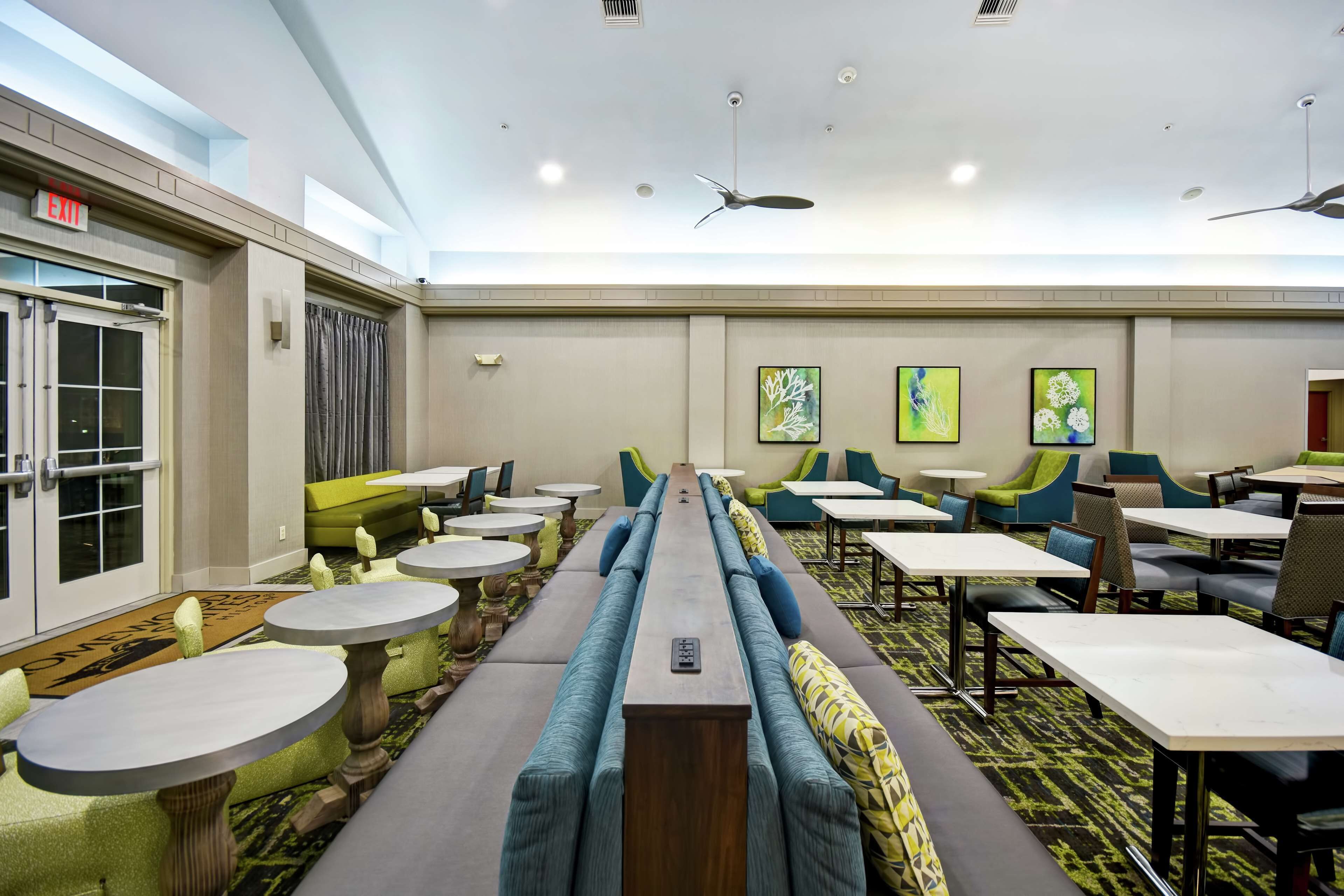 A hotel dining area with long communal tables, individual tables, and cushioned seating.