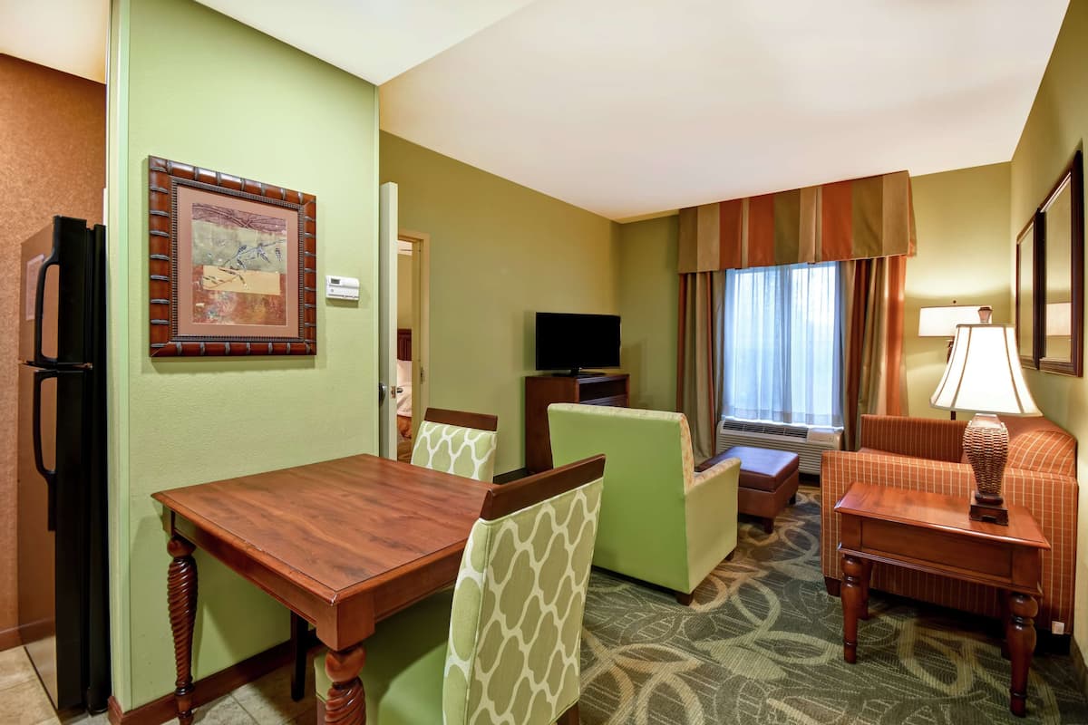 Habitación de hotel con una mesa de comedor, sillas, un sofá, un televisor y una lámpara.
