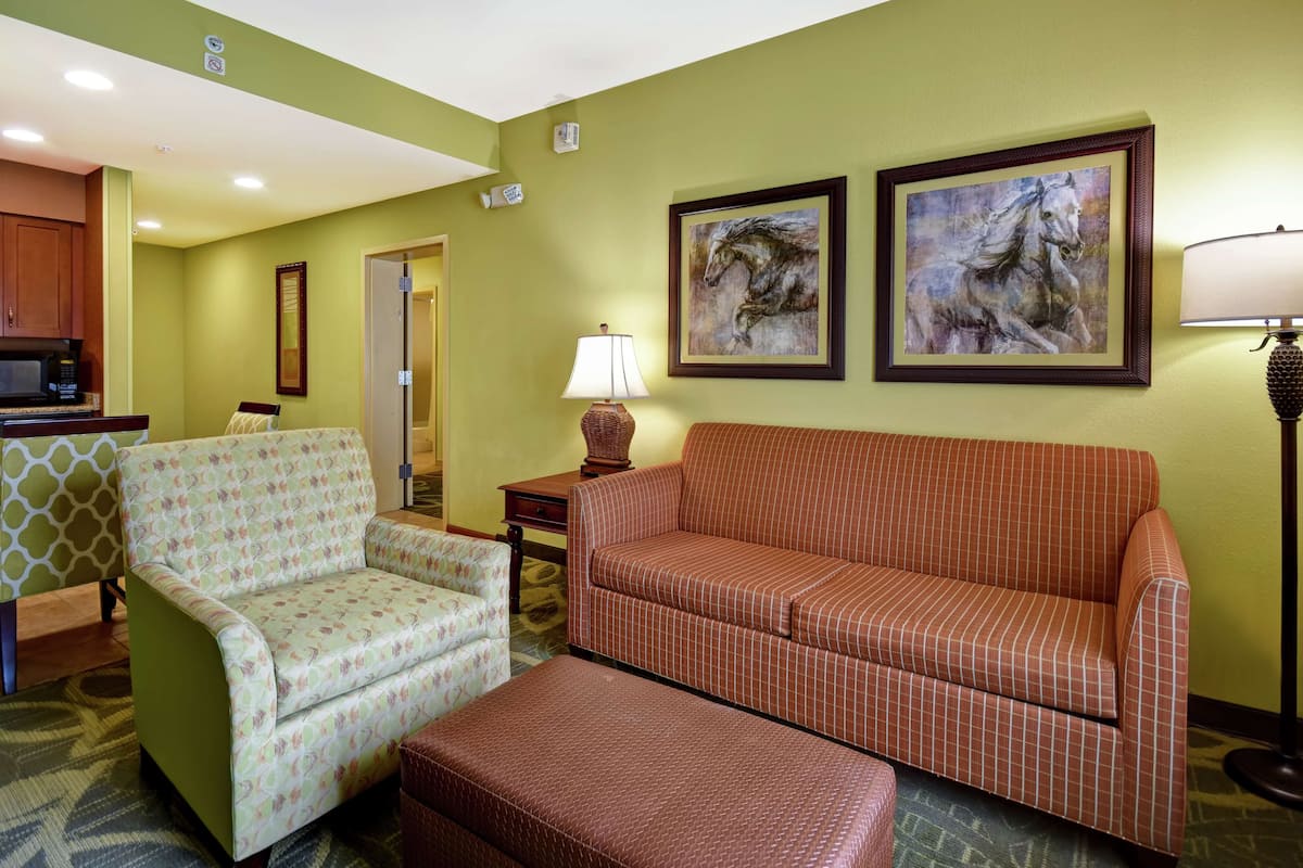 A living room with a sofa, armchair, and ottoman, a microwave, and two framed horse paintings on the wall.