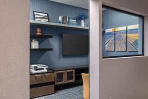 A modern office space with a flat-screen TV, shelves with books and decorative items, a printer, and a window with a view of fields. - Homewood Suites by Hilton Fresno (Fresno)