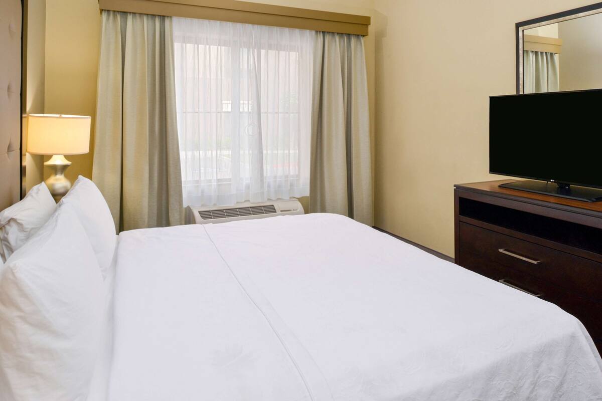 Ein Hotelzimmer mit Bett, Fernseher, Lampe und einem Fenster mit Vorhängen.