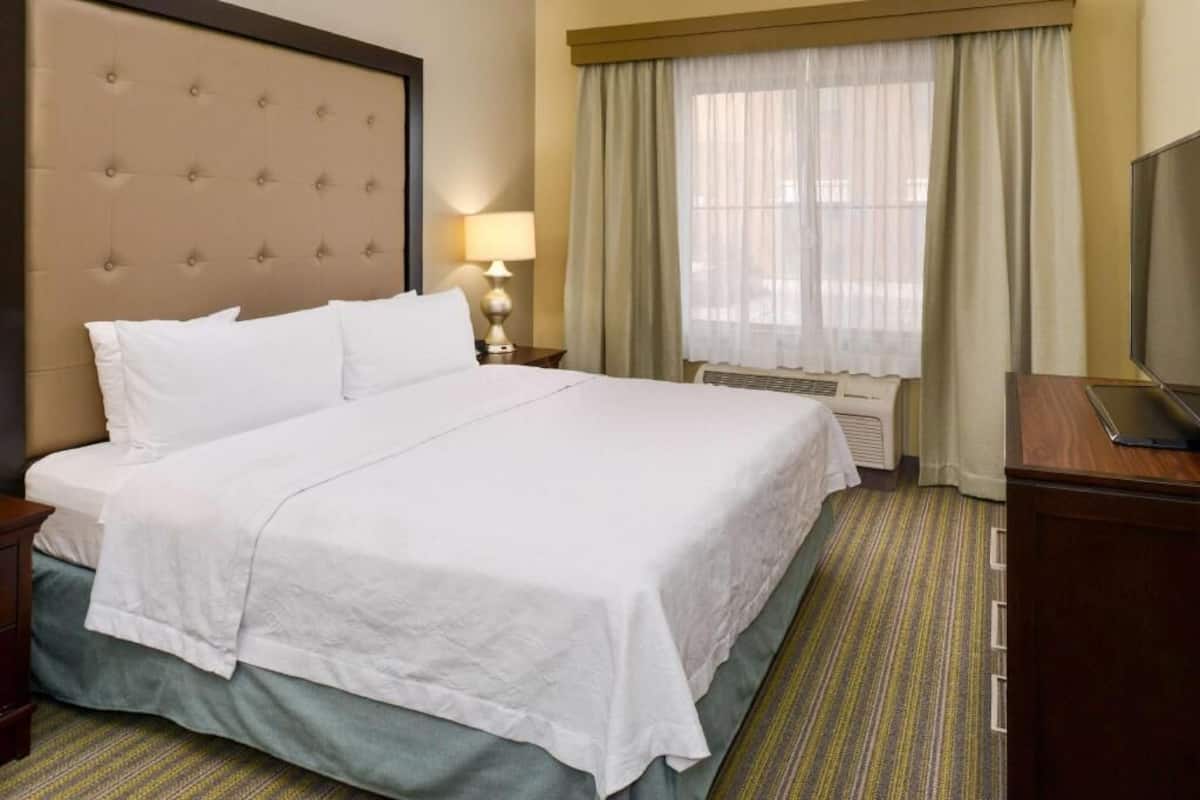 Ein Hotelzimmer mit einem großen Bett, einem Fernseher, einem Schreibtisch und einem Fenster mit Vorhängen.
