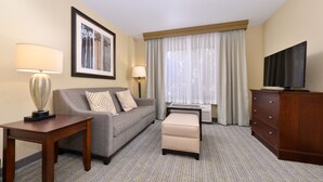 A hotel room with a sofa, a small table, a TV, a cabinet, and a large window with curtains.
