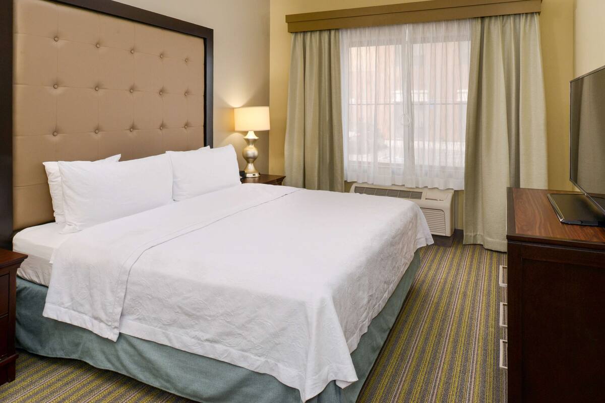 Ein Hotelzimmer mit einem großen Bett, einem Fernseher, einem Schreibtisch und einem fensterbepflanzten Fenster.