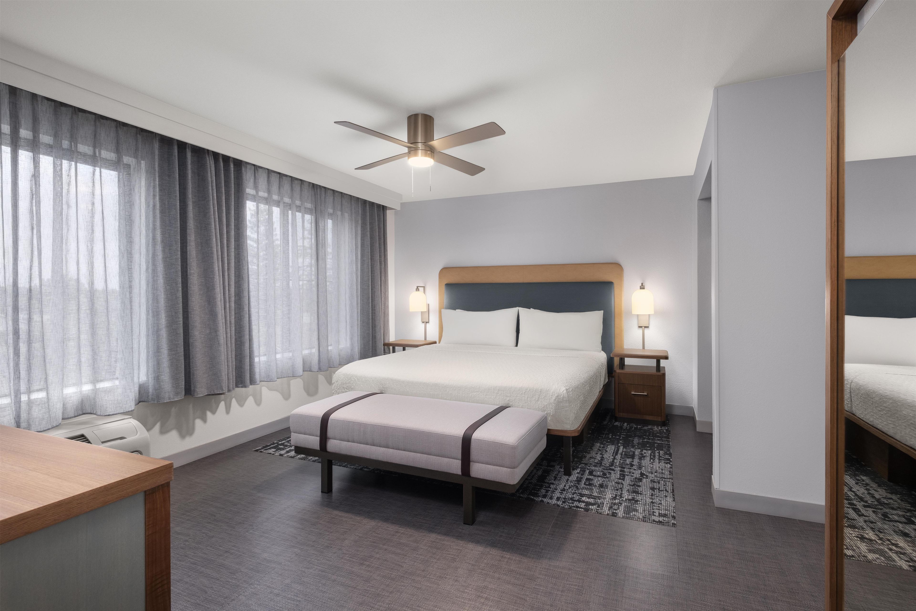 A hotel room with a bed, bedside tables, a desk, and a ceiling fan.
