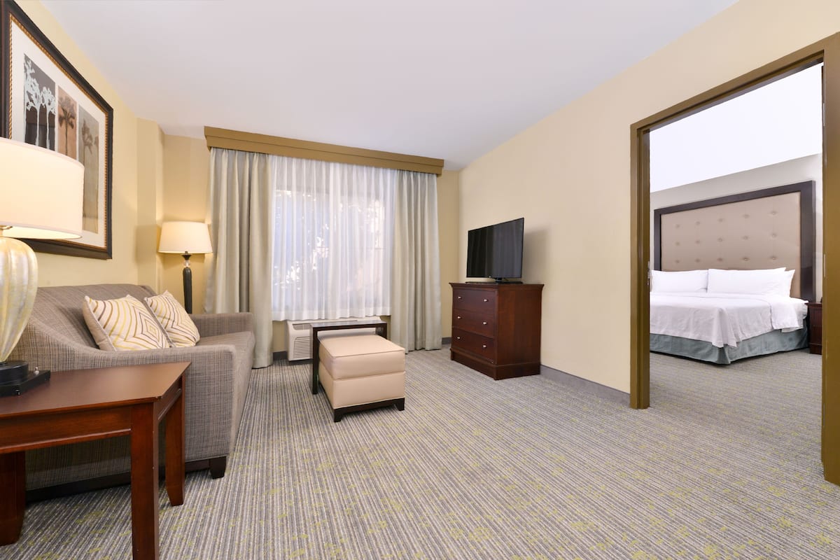 Ein Hotelzimmer mit Sofa, Hocker, Flachbildfernseher, Kommode und Bett.