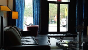 A modern hotel lobby with a sofa, armchair, and a small table with books. There is a large window with blue curtains, and an exit sign is visible. - The Ridge Hotel (New York)