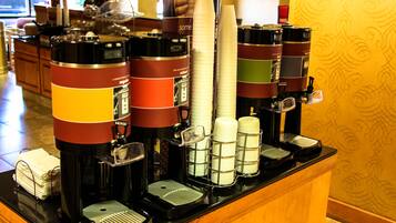 Uma estação de café com várias máquinas de café e uma pilha de copos descartáveis.