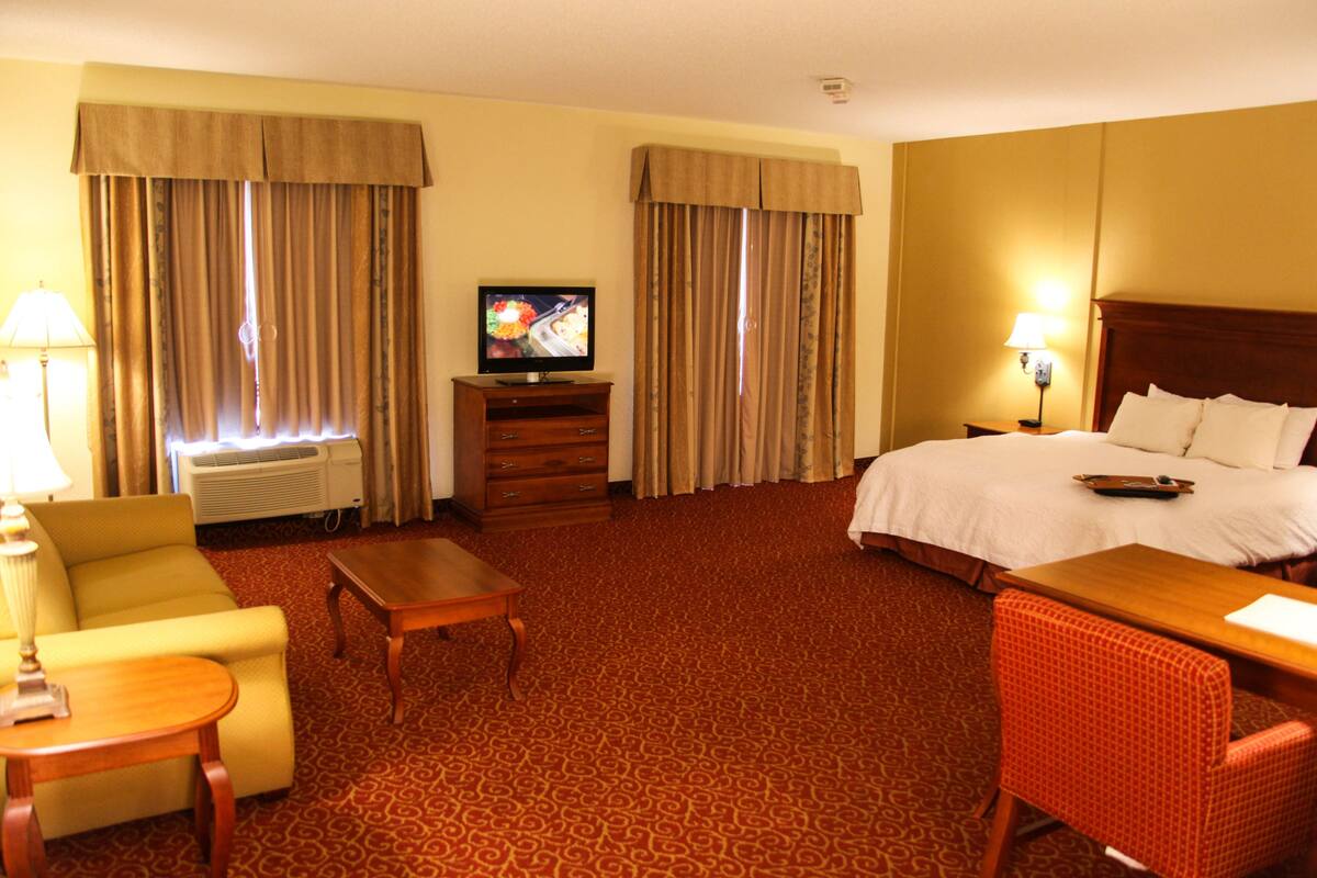 A hotel room with a bed, a television, a desk, a chair, and a lamp.