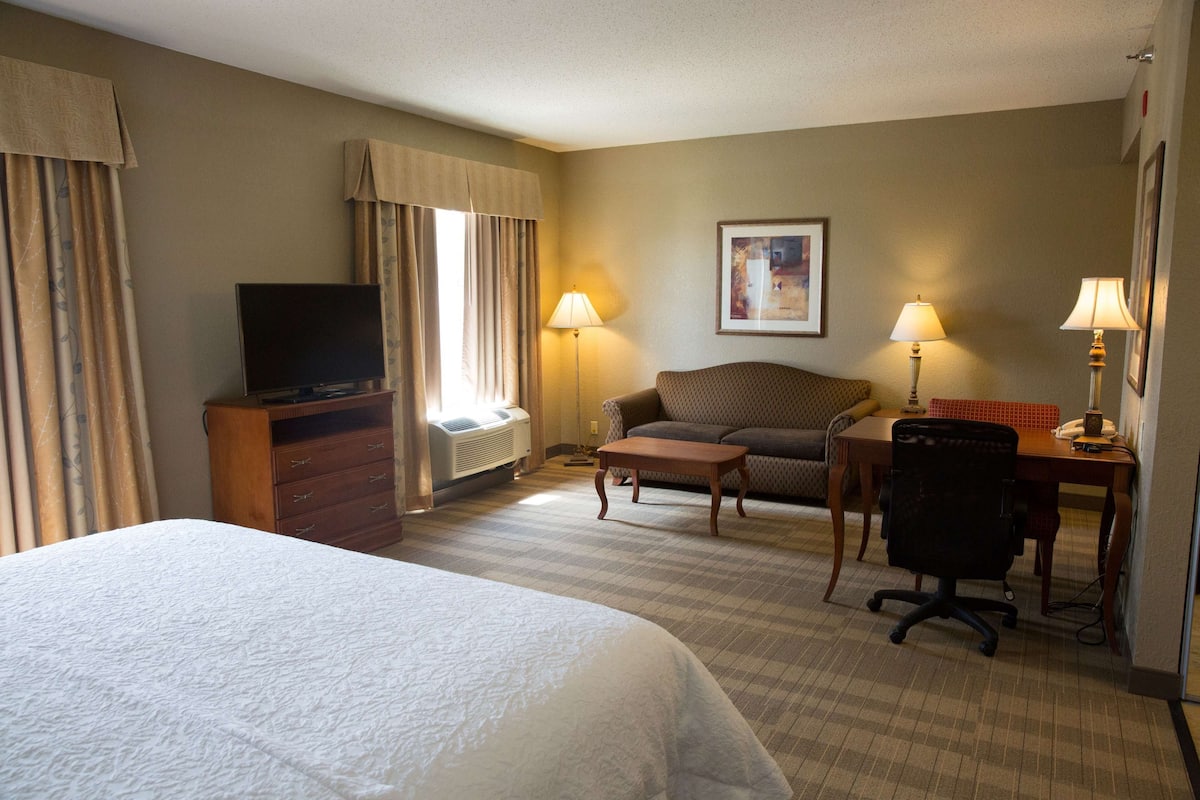 A hotel room with a large bed, a desk with a chair, a sofa, a television, and two lamps.