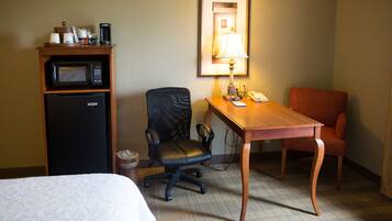 Une chambre d’hôtel comprenant un lit, un bureau avec une lampe, une chaise, un four à micro-ondes et une poubelle.