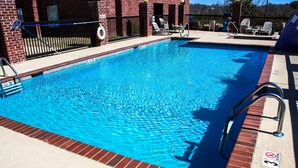Une piscine rectangulaire à l’eau d’un bleu limpide, entourée d’un mur de briques et d’une clôture en métal noir.