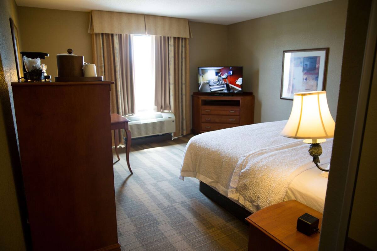 A hotel room with a bed, a television, a desk, a lamp, and a window with curtains.
